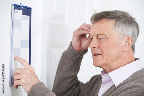 Confused Senior Man With Dementia Looking At Wall Calendar photo