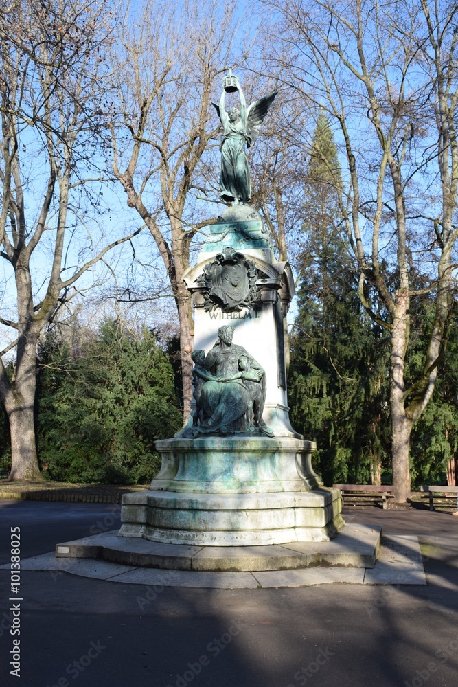 Statue eines Engels, der eine Krone hochhält, im Hintergrund blauer Himmel, Gesamtansicht
