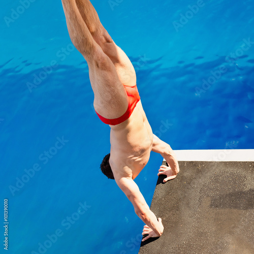 High diving competitor, starting a difficult dive from handstand. Shot from above
