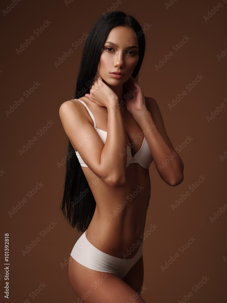 Naklejka premium Beautiful very slim girl with black straight hair is posing in the white basic seamless underwear collection in the studio