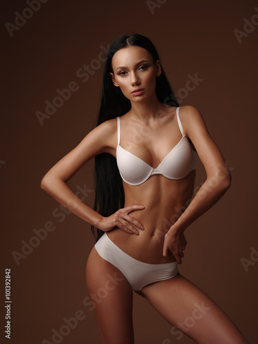 Foto de Skinny girl with black straight hair is posing in the white basic  seamless underwear collection in the studio do Stock