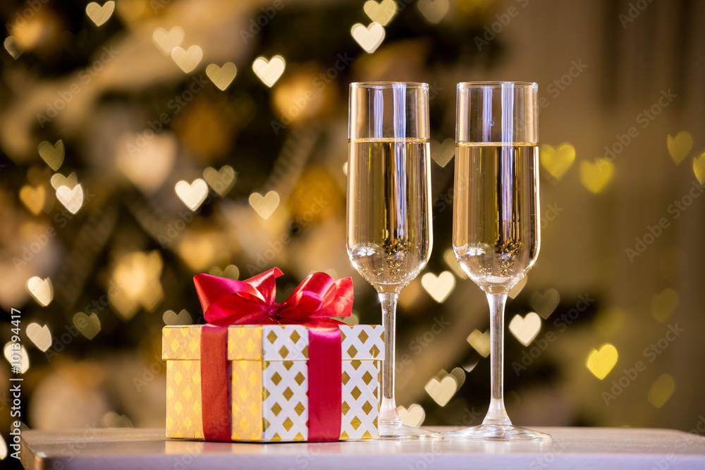 Two glasses of champagne and gift box with red bow. Background with blurred lights, bokeh of heart.
Two glasses of champagne and gift box with red bow. Background with blurred lights, bokeh of heart.