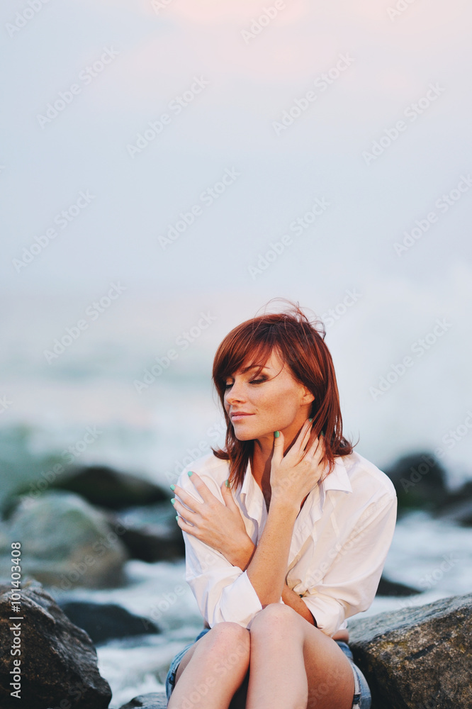 Молодая красивая девушка сидит на камнях на берегу моря 