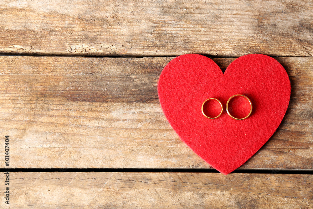 Red felt heart and wedding rings on wooden background closeup Red felt heart and wedding rings on wooden background closeup