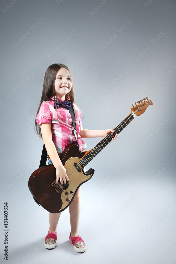 Beautiful artistic little girl playing guitar on grey background Beautiful artistic little girl playing guitar on grey background