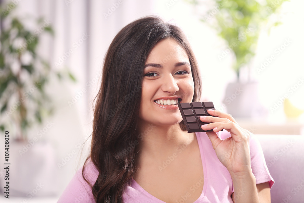 Portrait of beautiful young brunette with chocolate on sofa in the room , close up Portrait of beautiful young brunette with chocolate on sofa in the room , close up