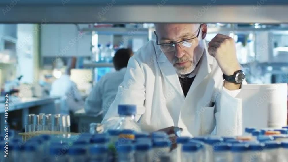 Senior scientist is sitting at the table in a laboratory and working with tube samples. Shot on RED Cinema Camera. Senior scientist is sitting at the table in a laboratory and working with tube samples. Shot on RED Cinema Camera.