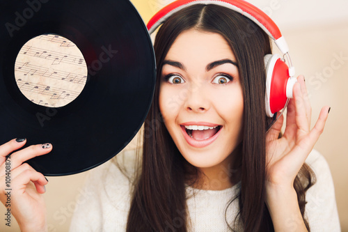 Happy young woman with headphones and vinyl record listening to music at home