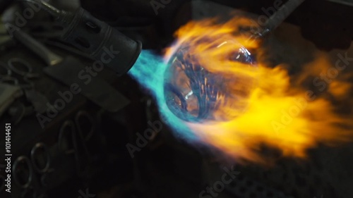 A glassmaker uses a blow torch to shape and form a glass object.