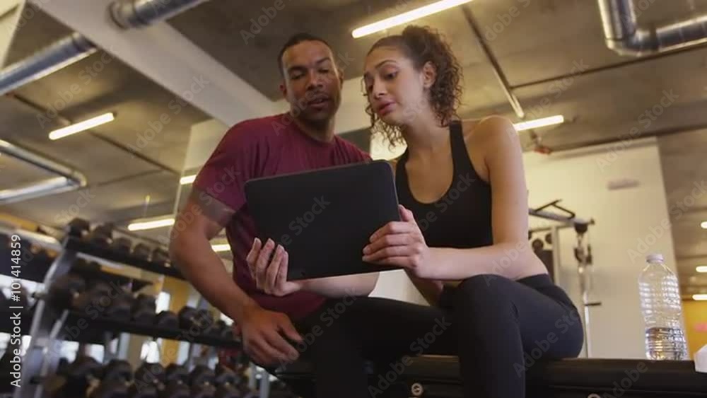 Happy fit Black and Hispanic couple using tablet computer in gym Happy fit Black and Hispanic couple using tablet computer in gym