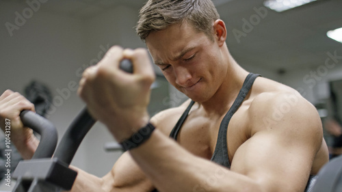 Obraz na plátně Handsome young man in the gym doing bicep curls on a machine