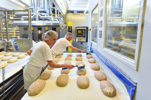 Arbeiter in einer Großbäckerei / Fliessband mit Brotlaibern am Backofen