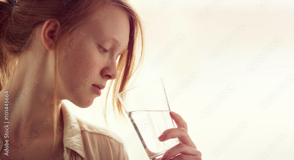 Young healthy redhead and freckled girl drinking a glass of water in bright bedroom. Young healthy redhead and freckled girl drinking a glass of water in bright bedroom.