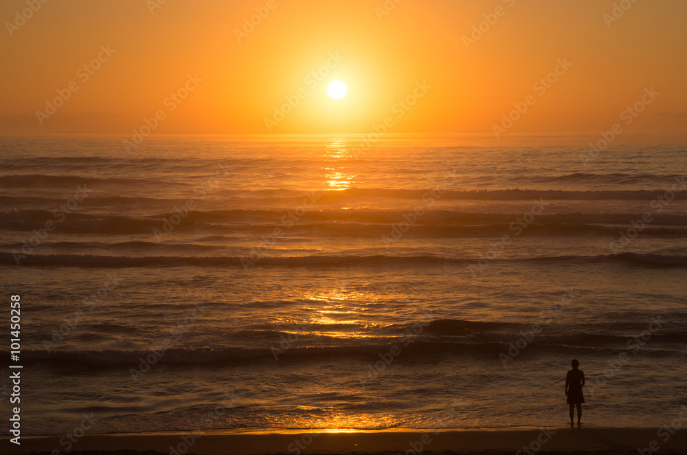 Sunset over the ocean with alone figure on the beach