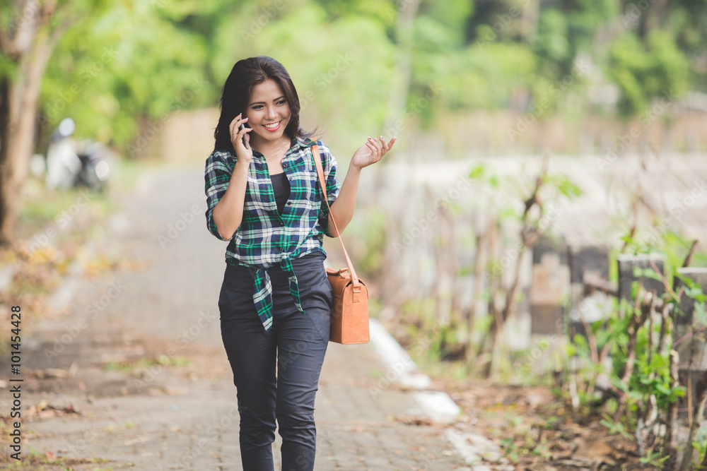 Εκτύπωση καμβά Young asian woman speaking on the phone while walking on the par