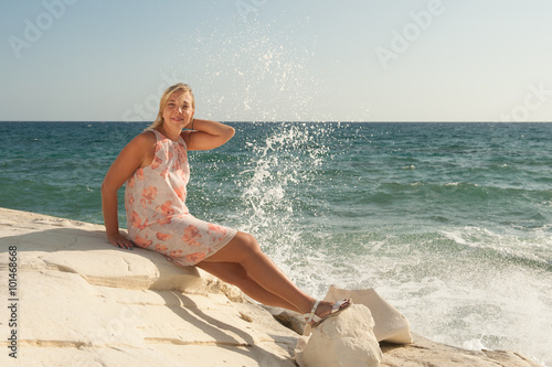 Young woman in summer dress sitting on the rocks by the sea photo