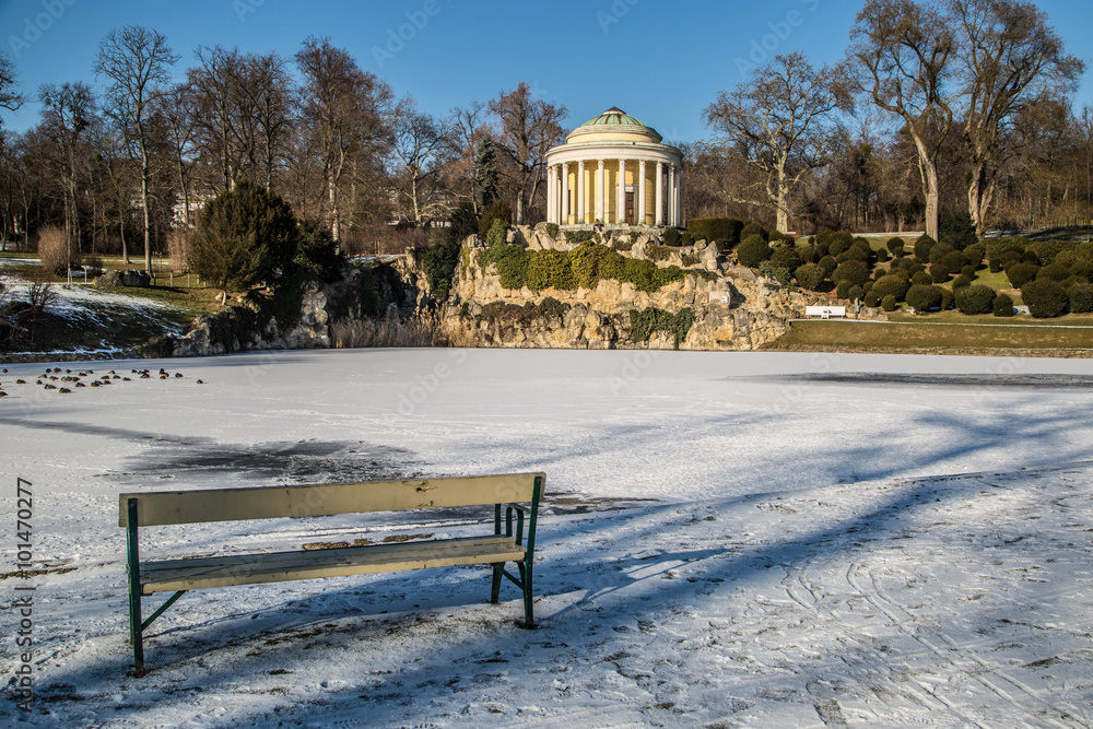 historischer Pavillon hinter gefrorenem See mit zahlreichen Enten