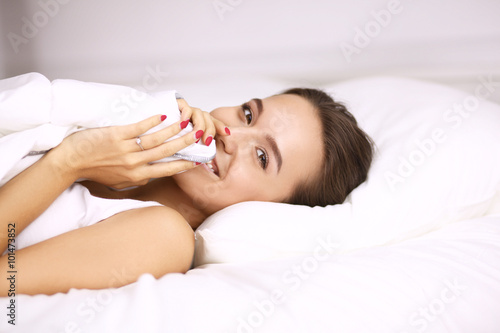 A pretty young woman peeking from under the covers in her bedroom happilly photo