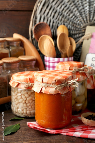 Jars with pickled vegetables and beans, spices, book of recipes and kitchen utensils on wooden background