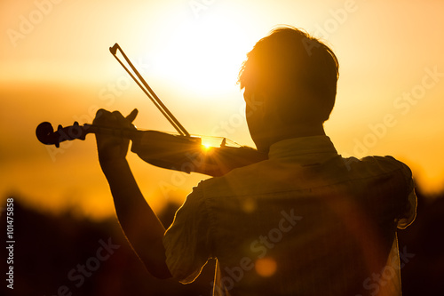 Young man or boy playing the violin at sunset