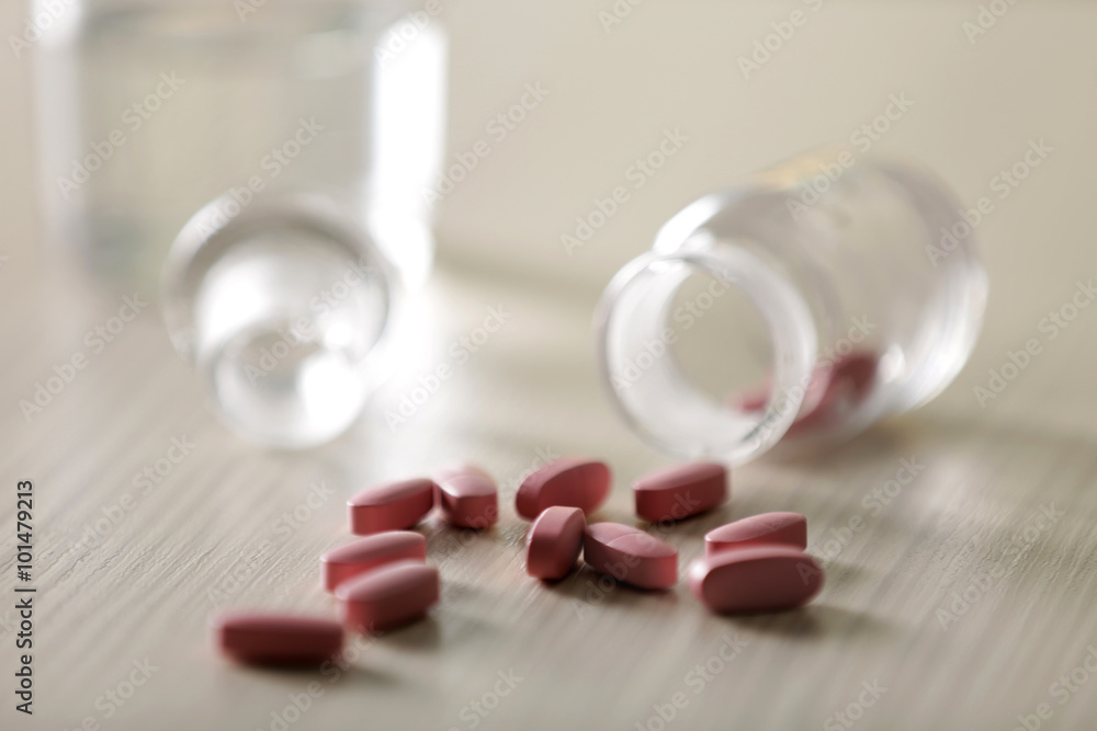 Pink capsules spilled from pill bottle and glass of water on the table, close up Pink capsules spilled from pill bottle and glass of water on the table, close up
