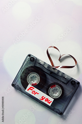 Audio cassette with magnetic tape in shape of hearts on light background