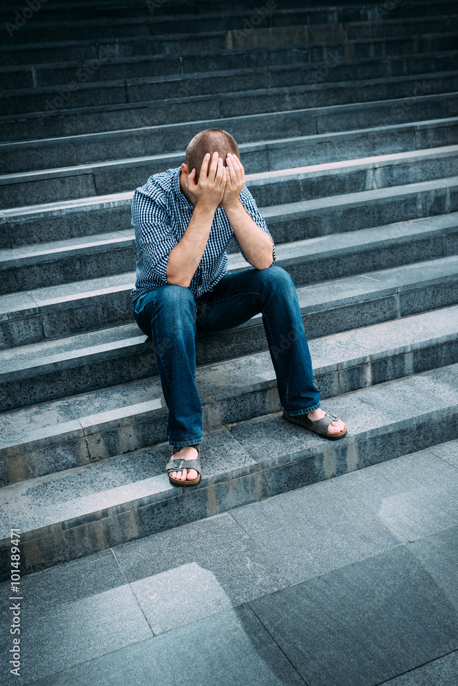 Outdoor portrait of despaired young man covering his face with hands sitting on stairs. Feelings of sadness, despair and tragedy Outdoor portrait of despaired young man covering his face with hands sitting on stairs. Feelings of sadness, despair and tragedy