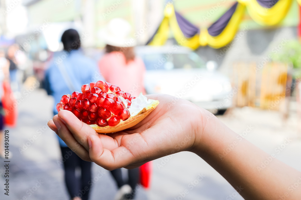 pomegranate in young girl hand with blurry people walking in the