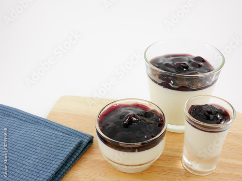 The tasty homemade blueberry panna cotta (Italian pudding dessert) in the small glass and blue cotton fabric on wooden board.