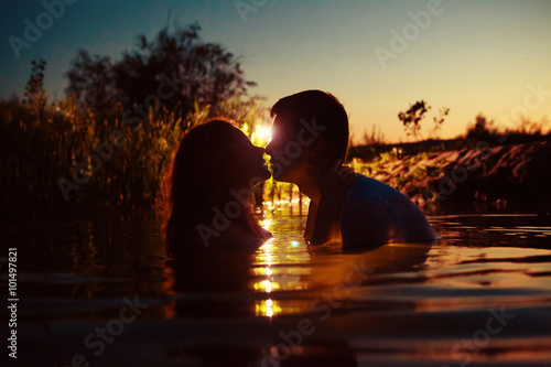 Young couple is kissing in the river on the summer sunset backgr