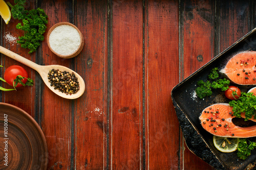 Raw salmon steaks on a wooden background. Ingredients for cooking: vegetables, spice and lemon. Rustic style. Top view. Selective focus