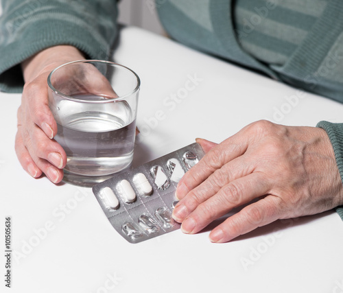  Senior woman with pills and glass of water at home