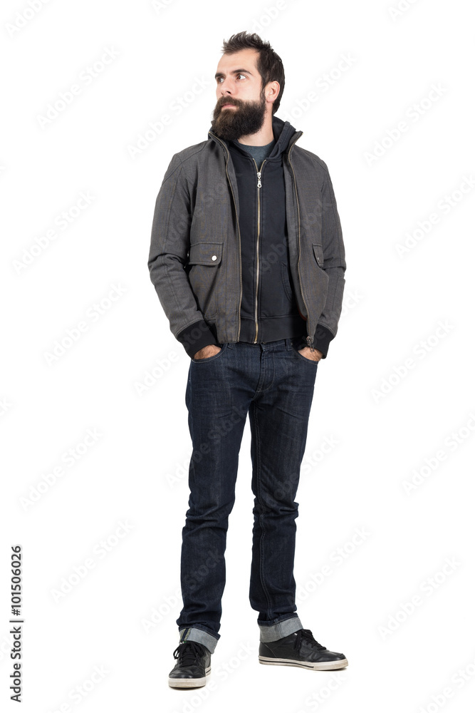 Confident stylish hipster wearing jacket over hooded sweatshirt looking away with hands in pockets. Full body length portrait isolated over white studio background. Confident stylish hipster wearing jacket over hooded sweatshirt looking away with hands in pockets. Full body length portrait isolated over white studio background.