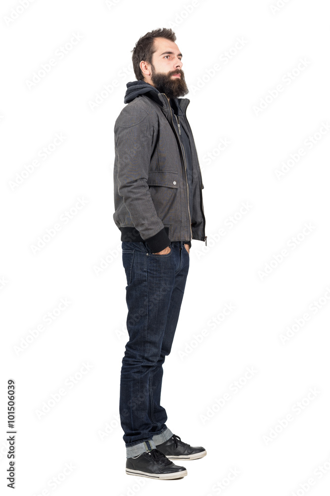 Side view of bearded man wearing jacket over hooded shirt looking away. Full body length portrait isolated over white studio background. Side view of bearded man wearing jacket over hooded shirt looking away. Full body length portrait isolated over white studio background.