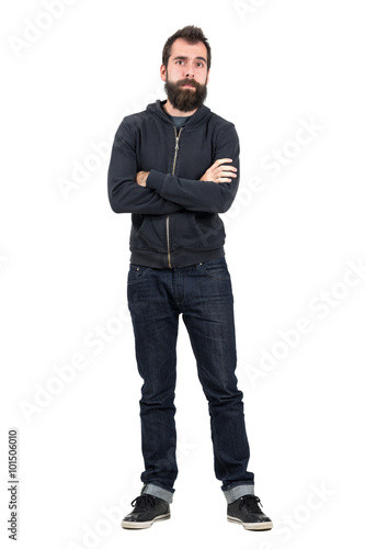 Skeptical hipster in black hooded sweatshirt with crossed arms looking at camera. Full body length portrait isolated over white studio background.