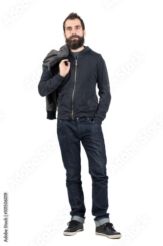 Serious hipster in hooded sweatshirt carrying jacket over the shoulder looking at camera. Full body length portrait isolated over white studio background.