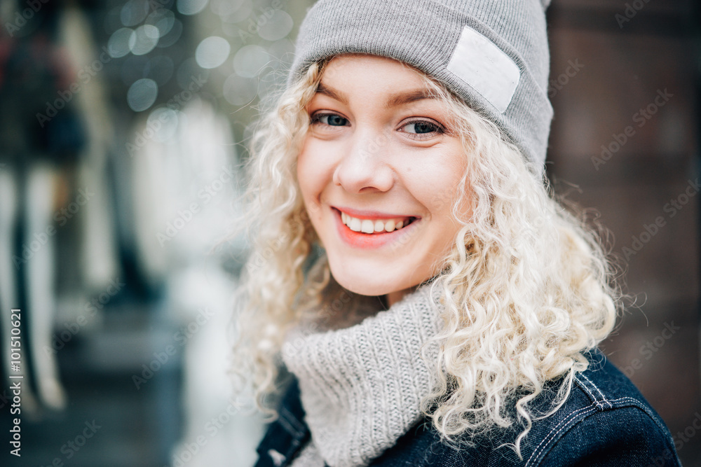 Portrait of young beautiful blond curly smiling girl in warm clothes in the street Portrait of young beautiful blond curly smiling girl in warm clothes in the street