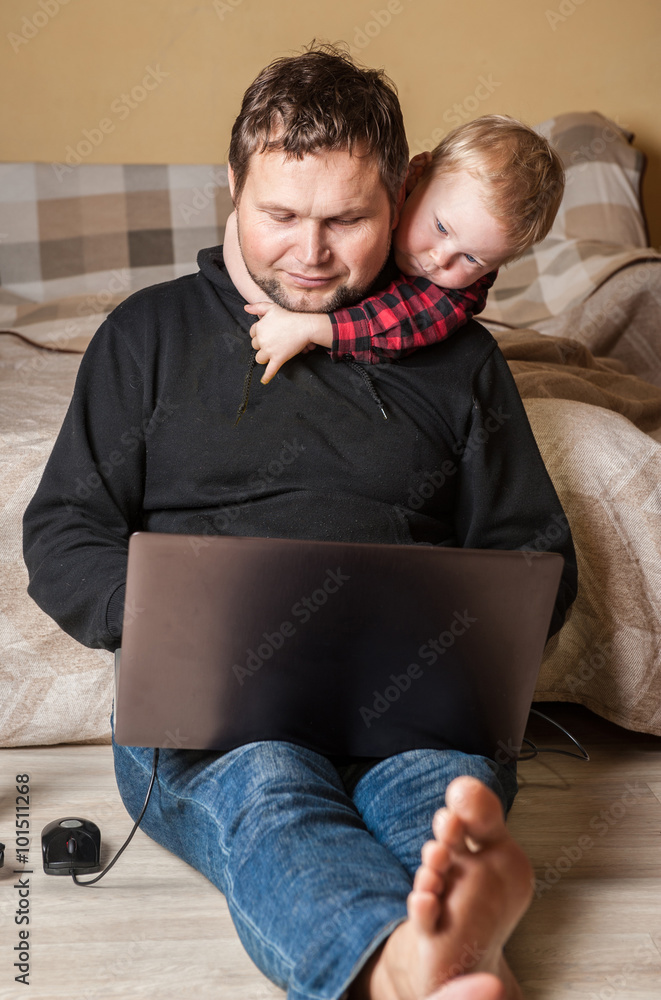 Fototapeta premium Young father working at home with computer and his child