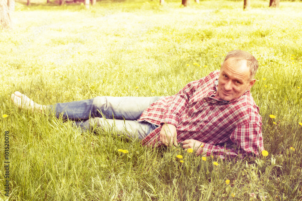 A man in a plaid shirt is resting lying on green grass. A man in a plaid shirt is resting lying on green grass.