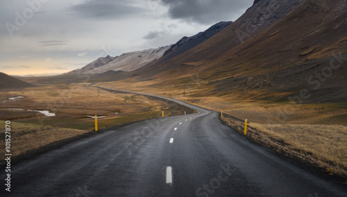 Dark asphalt road perspective with yellow field hill and mountain range background in Autumn season Iceland