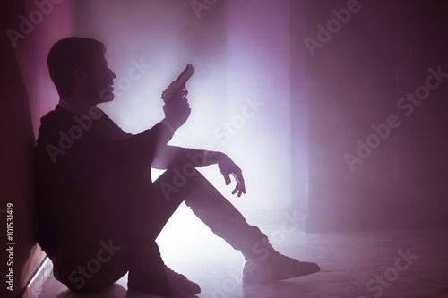 Silhouette of a Seated Man with a Gun. Real Smoke Effect. Shallow Deep of Field. Pink Filter Applied.