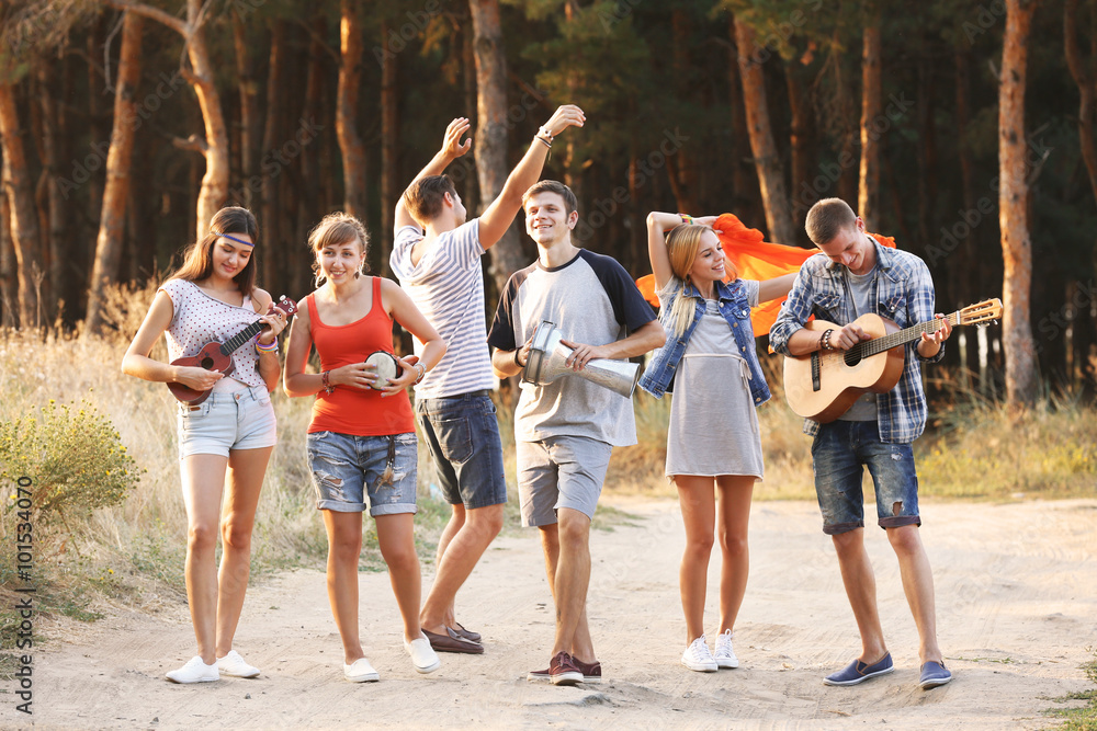 Obraz premium Happy smiling friends playing musical instruments in the forest outdoors