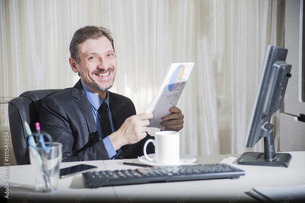 serious businessman sitting at his desk and smiles serious businessman sitting at his desk and smiles