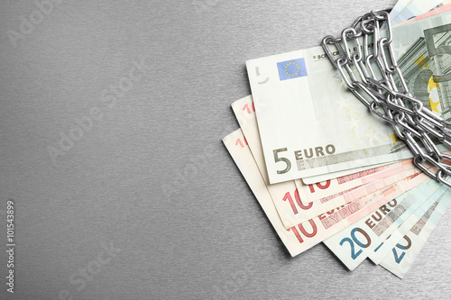 Euro banknotes with lock and chain on gray background
