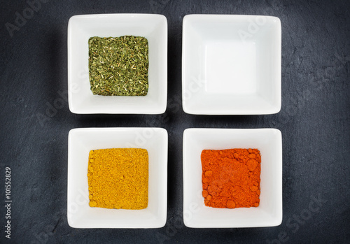 three bowls with spices and a blank one on grey background