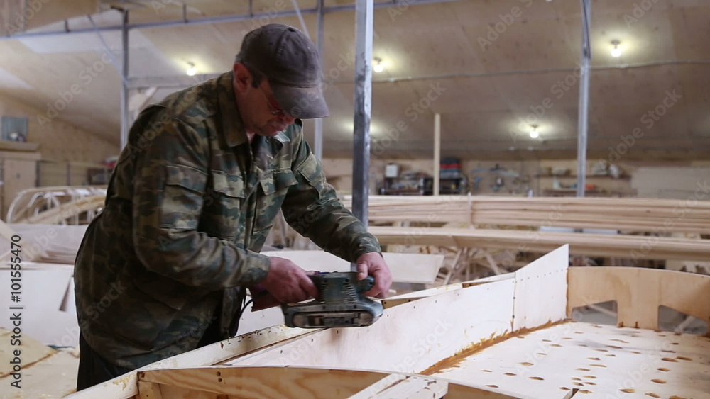 A carpenter polishes details wooden boat belt sander machine in the construction of boats at the shipyard
A carpenter polishes details wooden boat belt sander machine in the construction of boats at the shipyard