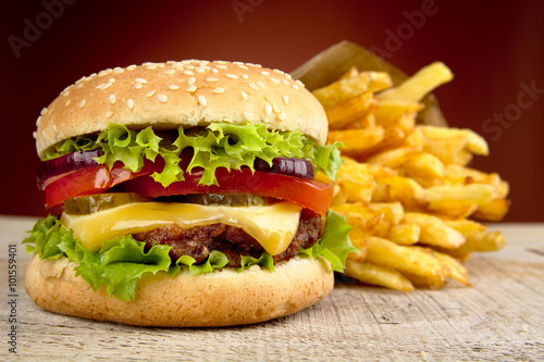 Cheeseburger and french fries on red spotlight on wooden table