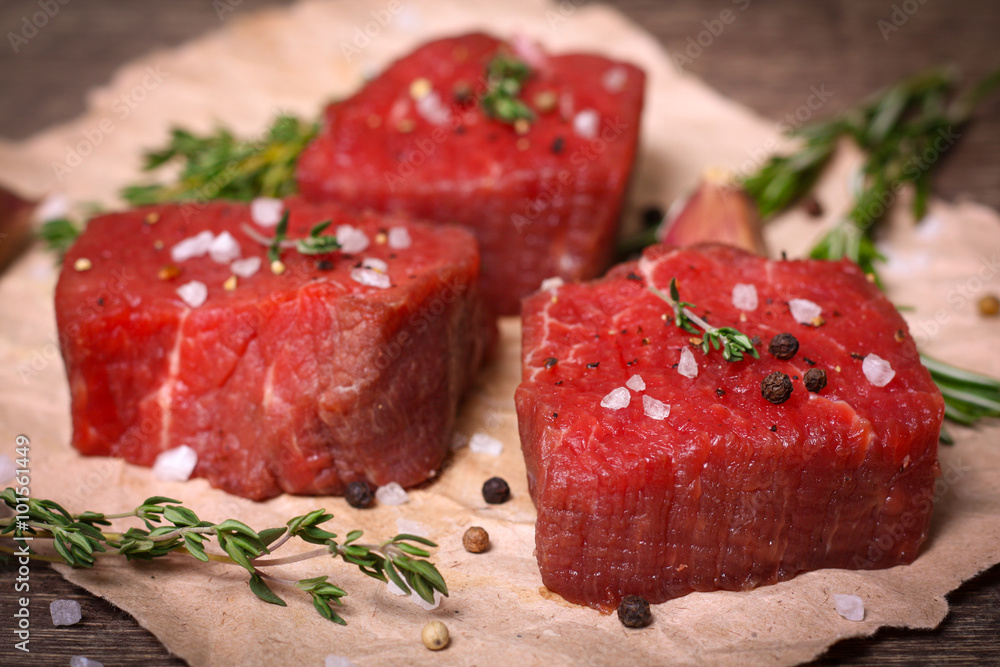 Raw beef steak with rosemary, thyme and garlic on wooden background Raw beef steak with rosemary, thyme and garlic on wooden background