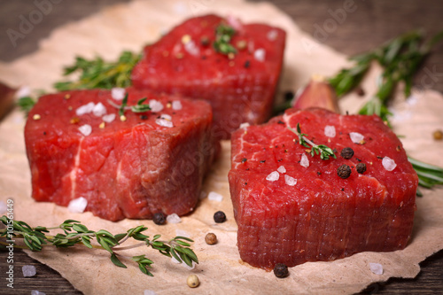 Raw beef steak with rosemary, thyme and garlic on wooden background