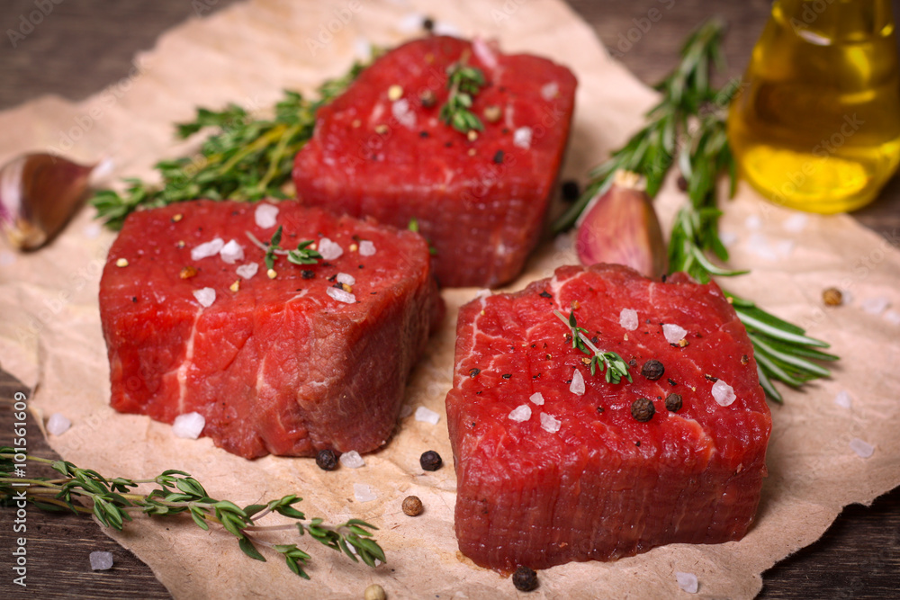 Raw beef steak with rosemary, thyme and garlic on wooden background Raw beef steak with rosemary, thyme and garlic on wooden background